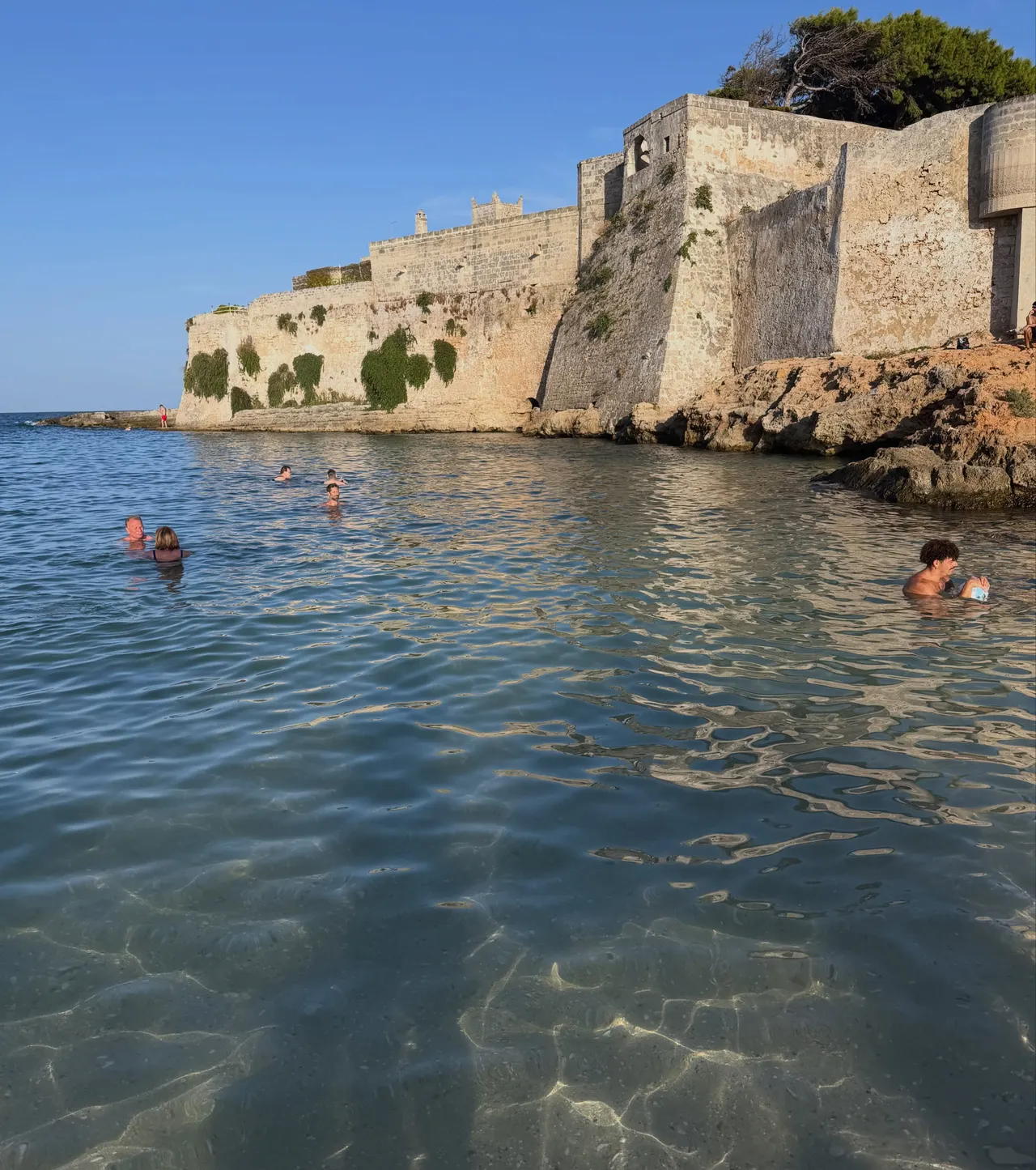 Swimmers in the sea below old fortress walls at golden hour