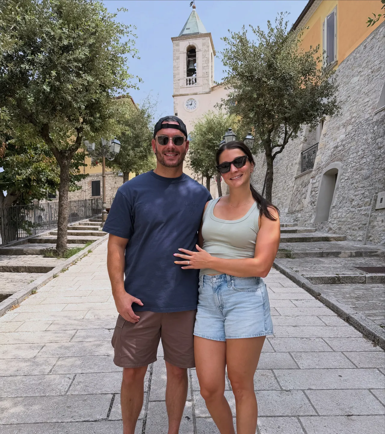 Drew and Valerie in a village square with a bell tower behind them