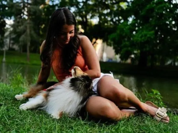 Valerie sitting on the grass beside a canal with her Sheltie