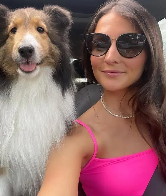 Valerie in a pink top taking a selfie in the car with her Sheltie