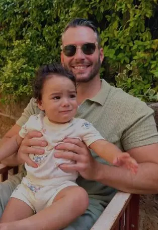 Drew in sunglasses holding a toddler in a garden